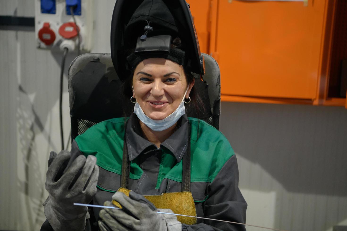 Eine Frau, die in einer modernen Fabrik zur Herstellung und Verarbeitung von Metallen in einer Arbeitsuniform beschäftigt ist, schweißt Metallmaterialien foto