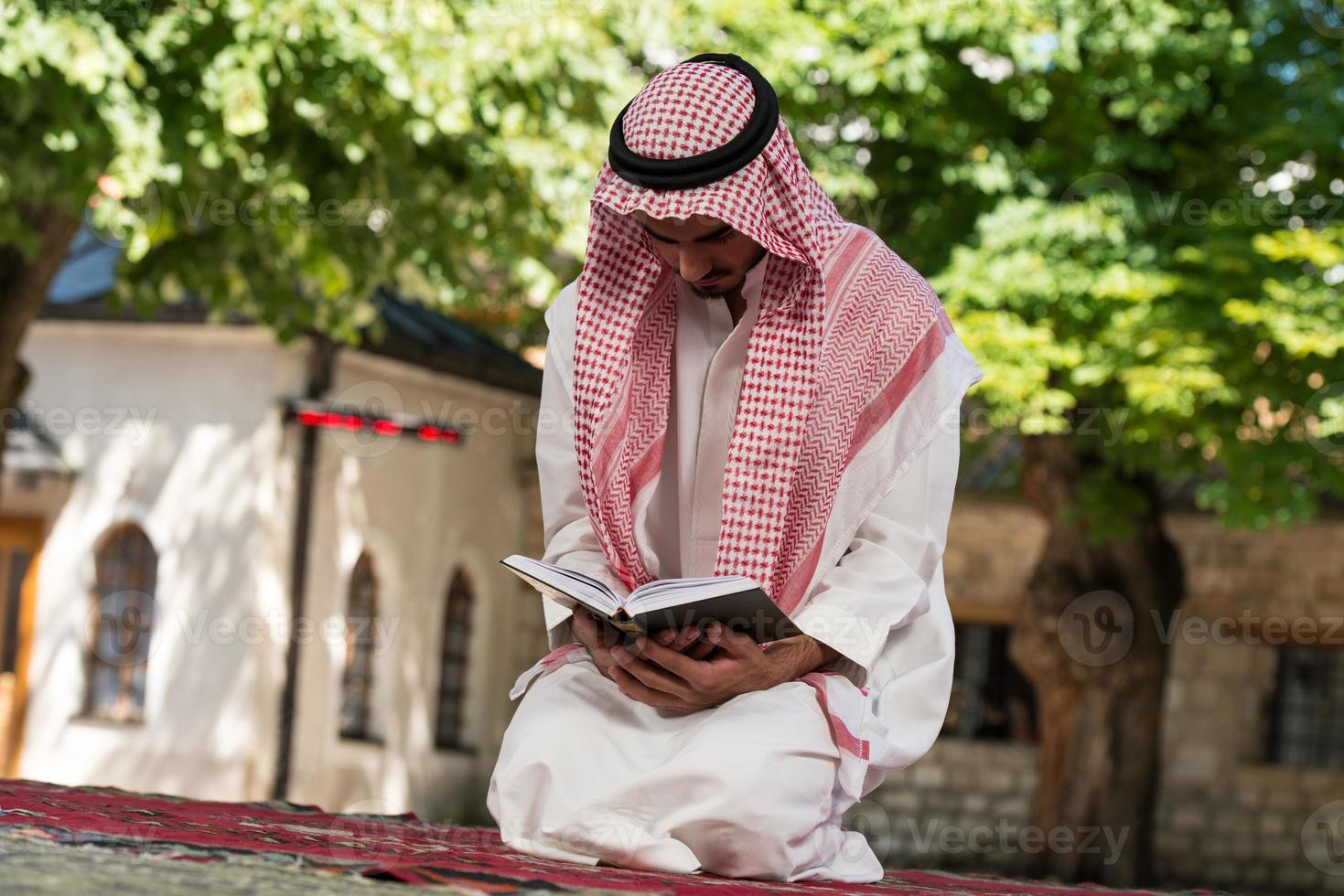 Der muslimische Mann in Dishdasha liest den Koran foto