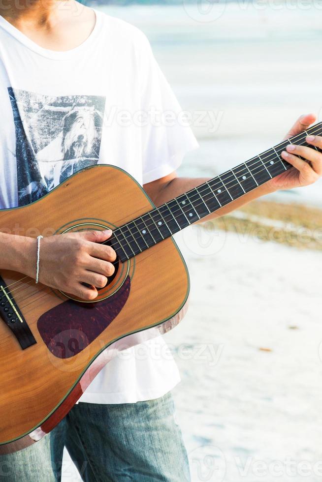 junger Mann, der Gitarre am Strand spielt foto