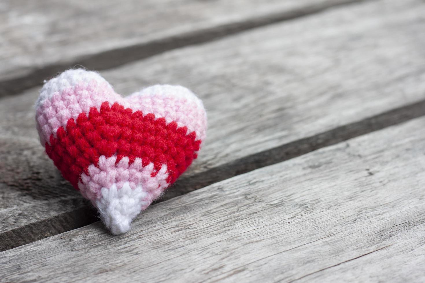 Gehäkelte bunte Herzform aus Garn auf Vintage-Holztischhintergrund zum Valentinstag. foto