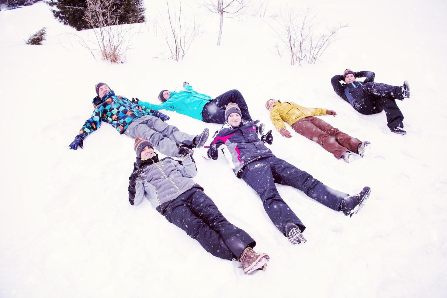 gruppe junger leute, die auf schnee legen und schneeengel machen foto