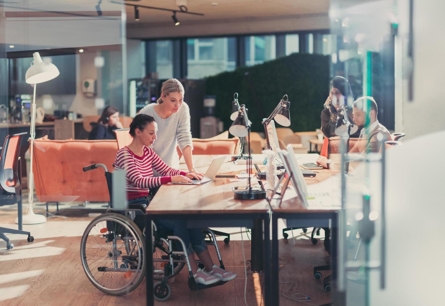 Behinderte Geschäftsfrau im Rollstuhl in modernen Coworking-Büroräumen. Kollegen im Hintergrund. Behinderungs- und Behinderungskonzept. selektiver Fokus foto