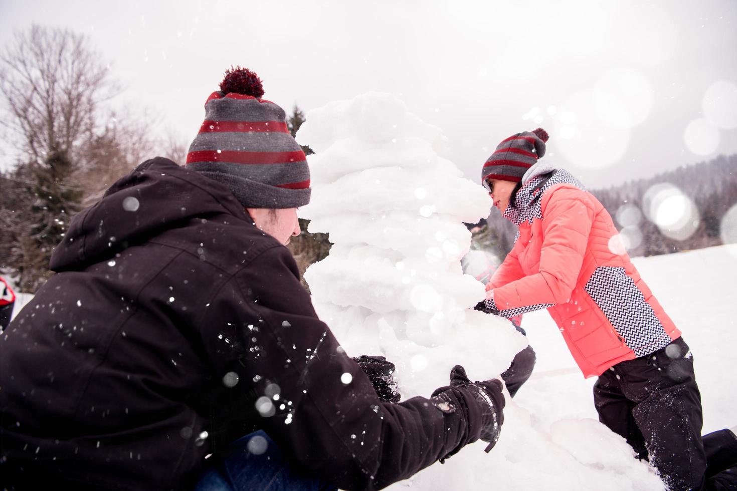 Gruppe junger Leute, die einen Schneemann bauen foto