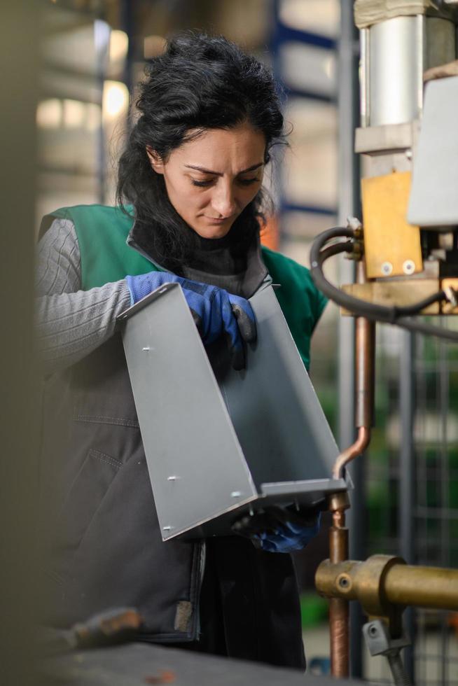 Eine Frau, die in einer modernen Metallfabrik arbeitet, montiert Teile für eine neue Maschine foto