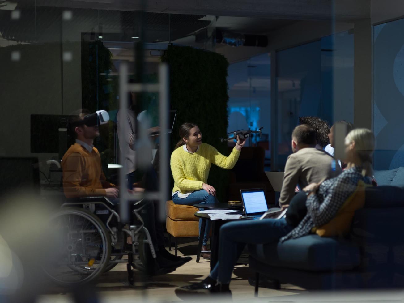 Behinderter Geschäftsmann im Rollstuhl bei der Arbeit in einem modernen Open-Space-Coworking-Büro mit Team, das Virtual-Reality-Googles-Drohnenunterstützungssimulation verwendet foto