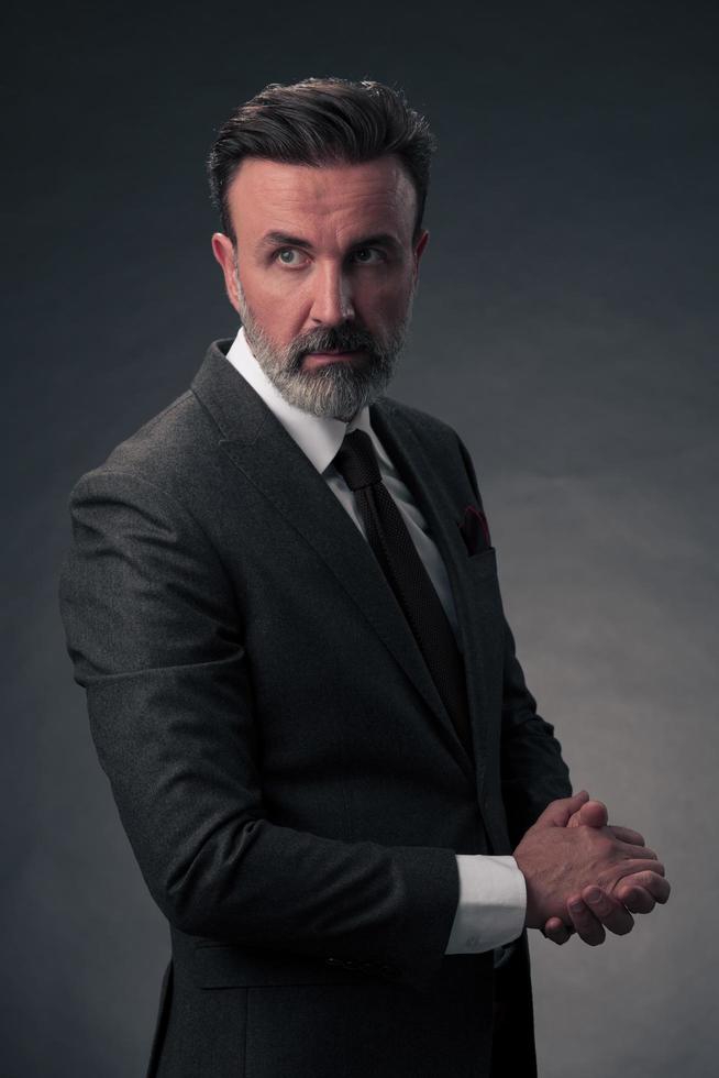 Porträt eines stilvollen, eleganten Senior-Geschäftsmanns mit Bart und lässiger Geschäftskleidung im Fotostudio isoliert auf dunklem Hintergrund, der mit den Händen gestikuliert foto