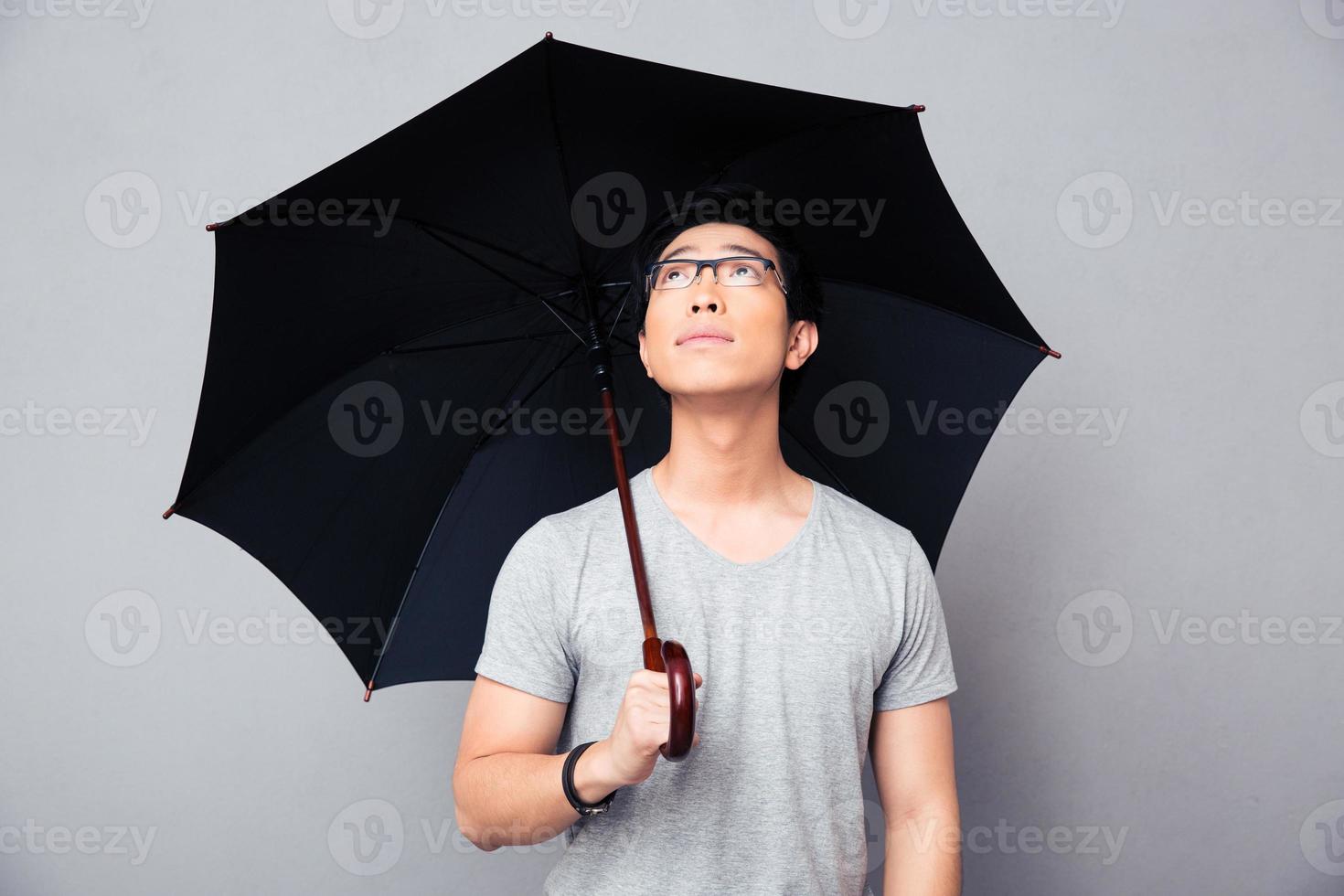 asiatischer Mann, der mit Regenschirm steht und aufschaut foto