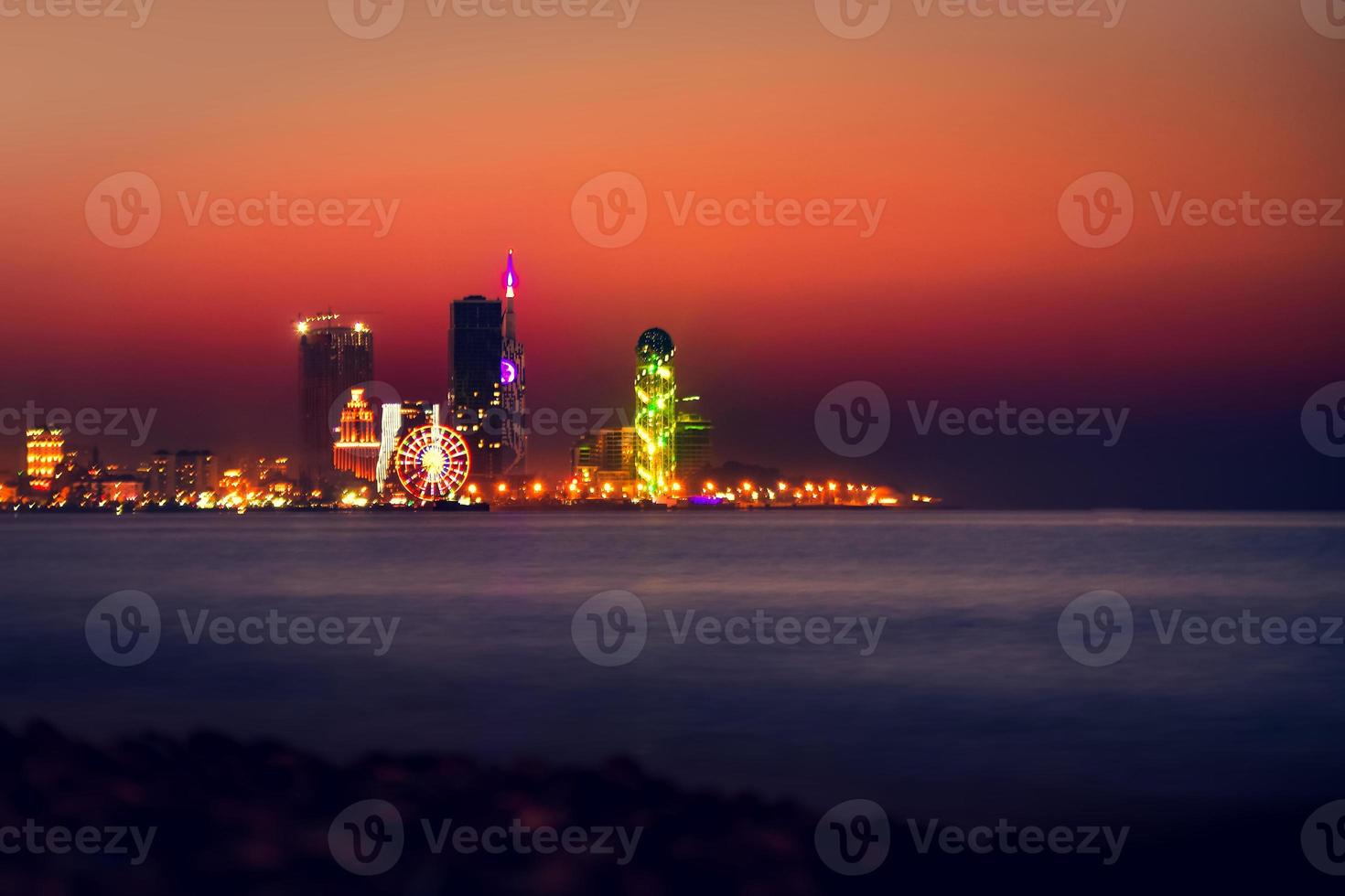 Nachtstadt Batumi blaue Stunde mit Panorama am Wasser. Batumi, Adscharien, Georgien. Panorama der beleuchteten Kurstadt bei Sonnenuntergang. Schwarzes Meer, Riesenrad und Alphabetturm foto