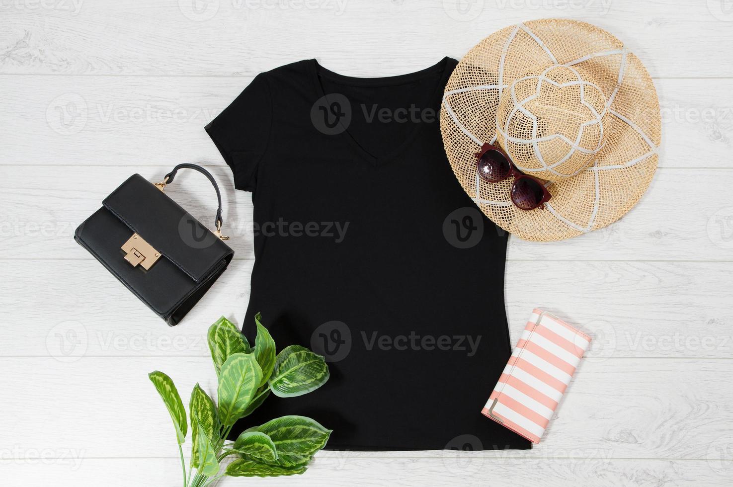 T-Shirt schwarz. t-shirt-modell flach gelegt mit sommeraccessoires. hut, tasche und sonnenbrille auf holzbodenhintergrund. Platz kopieren. Vorlage leere Leinwand. Vorderansicht von oben. foto