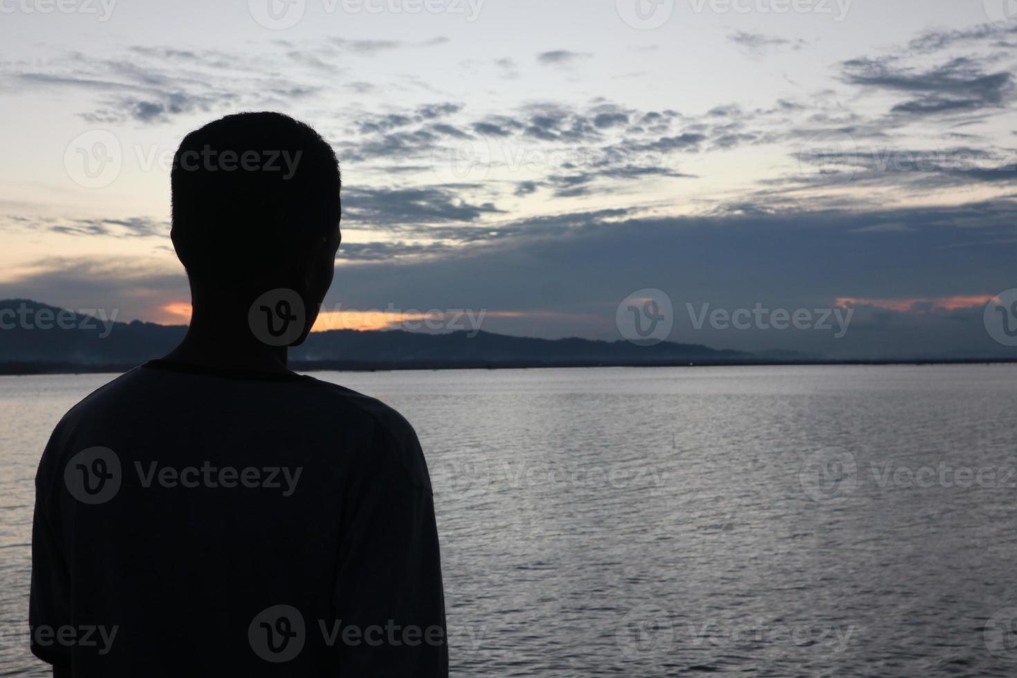 Silhouette eines jungen Mannes, der am See steht und den Sonnenuntergang genießt. friedliche Atmosphäre in der Natur foto