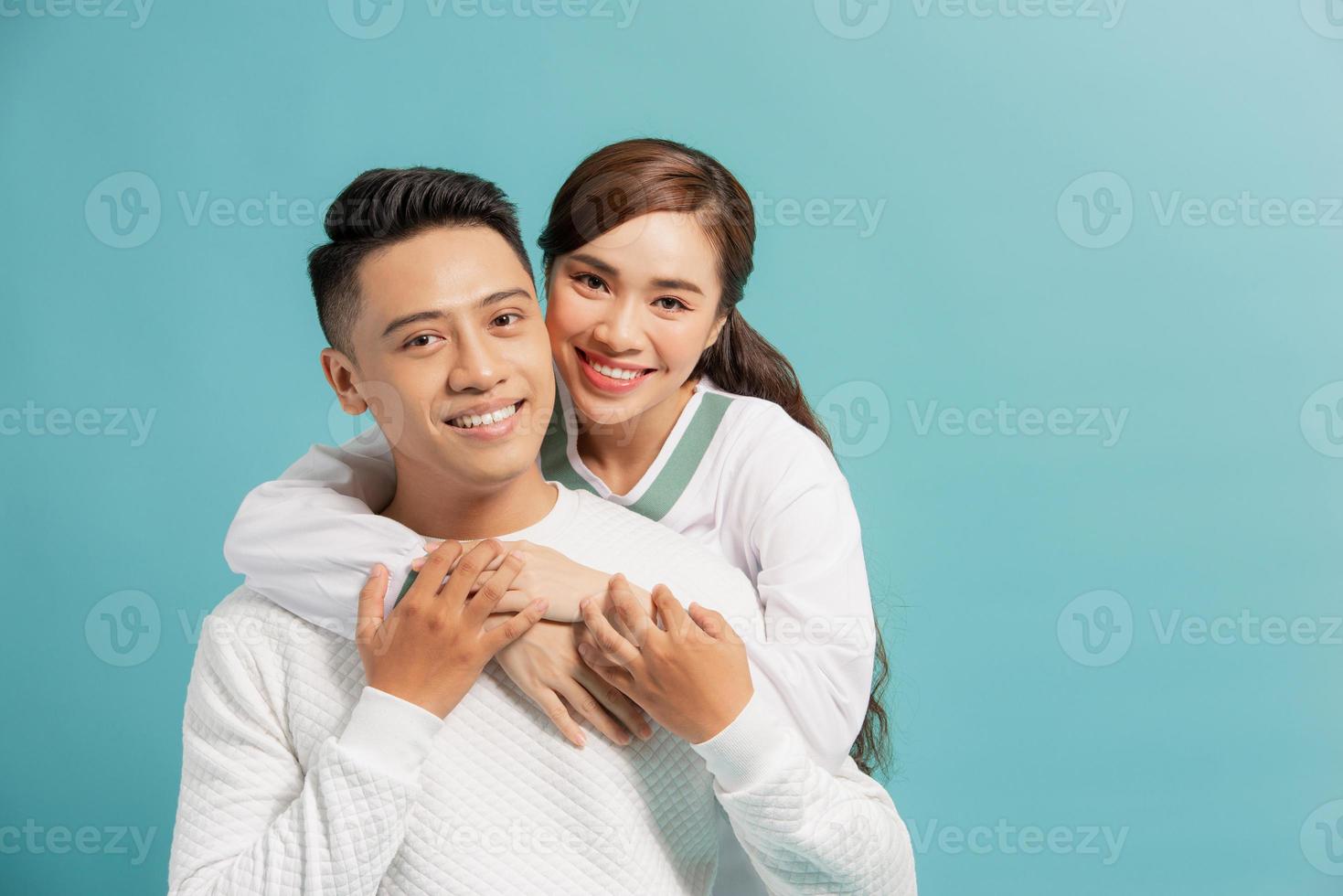 Porträt eines schönen jungen Paares, das sich umarmt, in die Kamera schaut und lächelt, isoliert auf blau foto