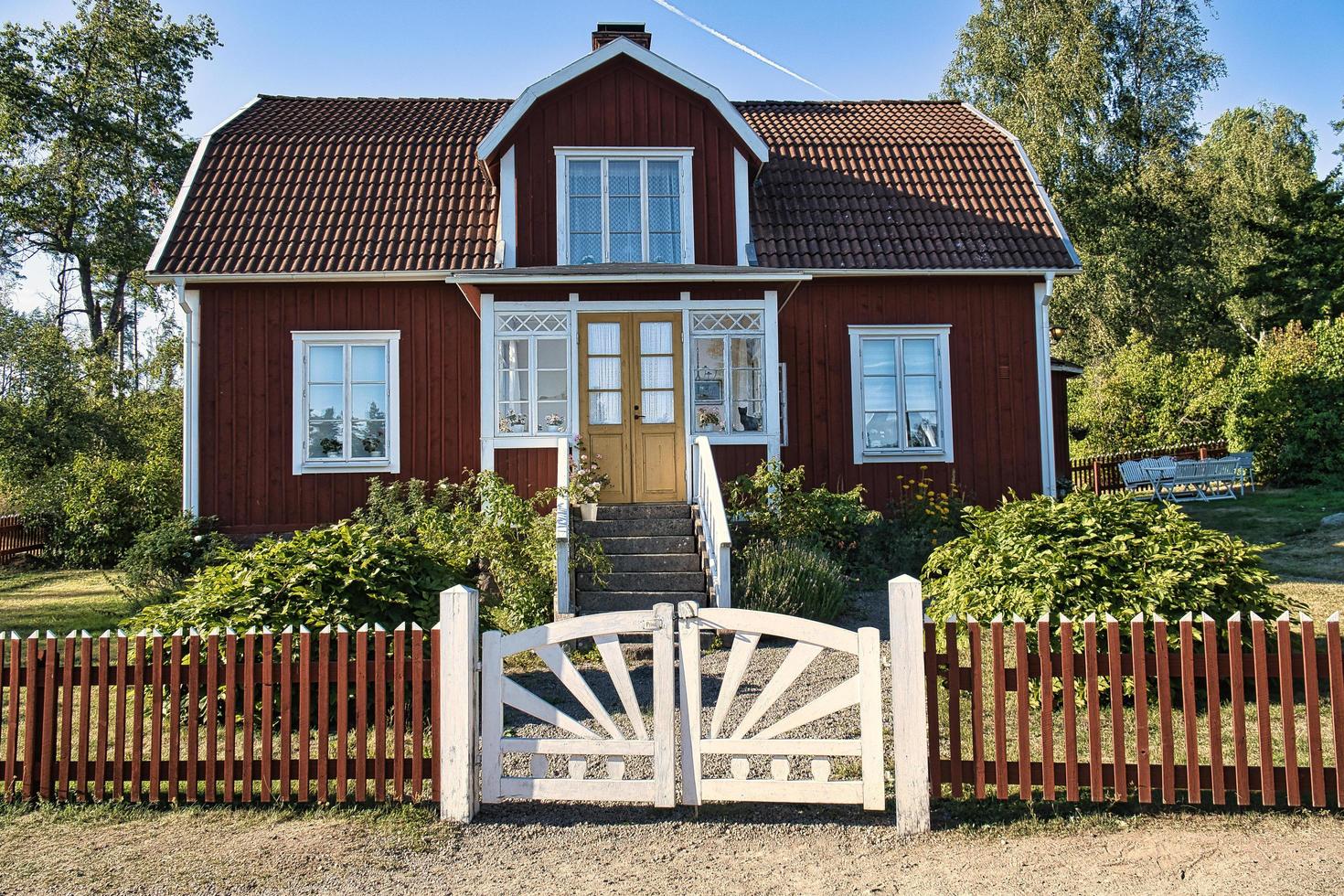 schwedisches rotes und weißes traditionelles haus in kleinem, weißem zaun grüner garten blauer himmel foto