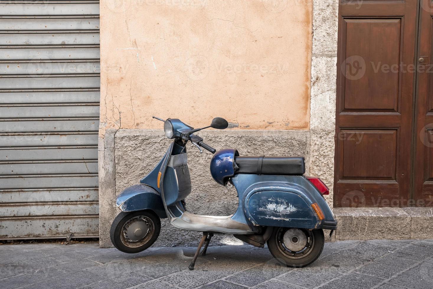 Blauer alter Roller, der auf der Straße mit Haus im Hintergrund in der Stadt geparkt ist foto