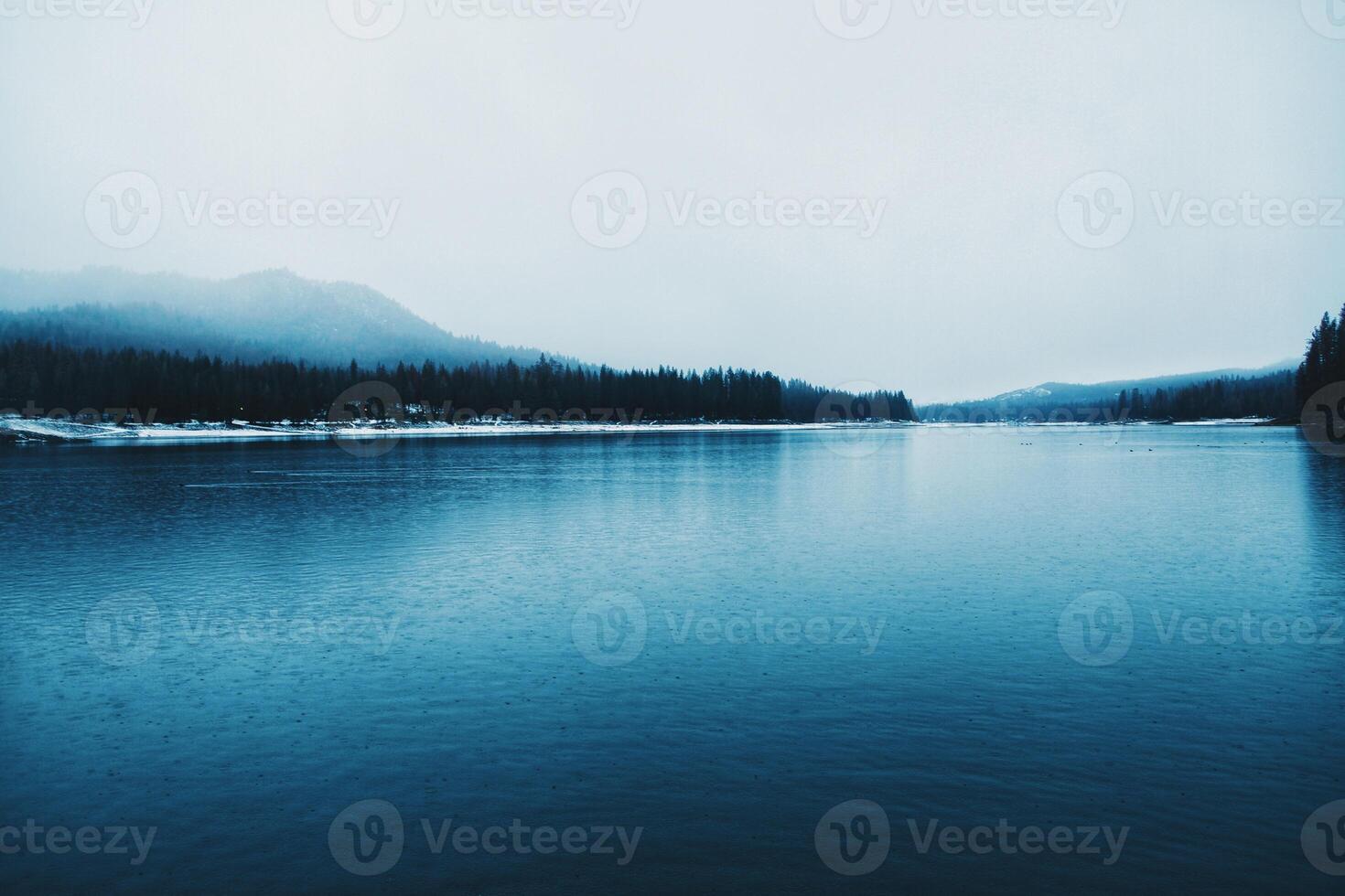 die Oberfläche eines Sees im Winter mit einem bewaldeten Hügel am nebligen Horizont foto