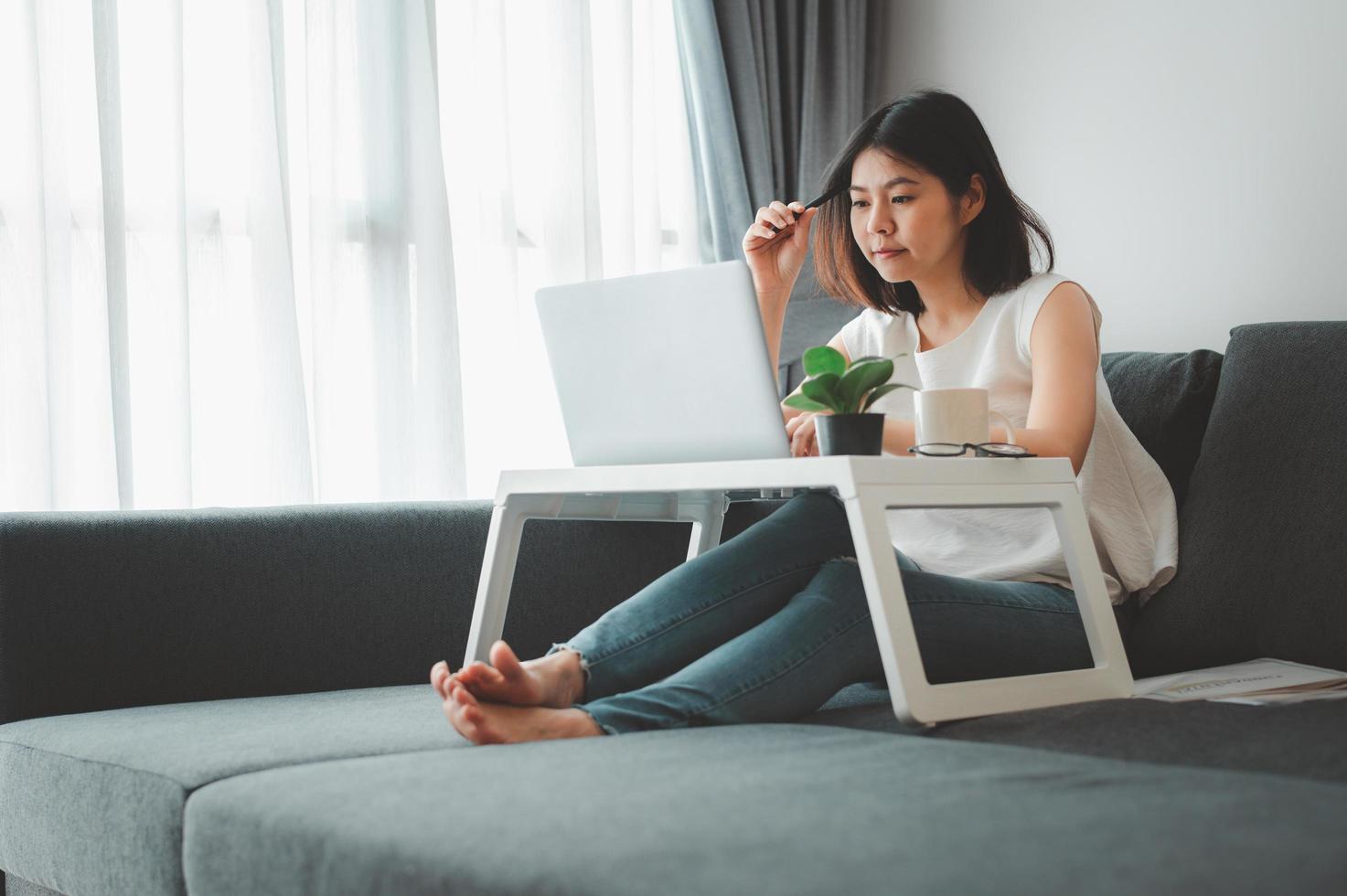 Frau denkt, während sie zu Hause auf dem Sofa arbeitet foto