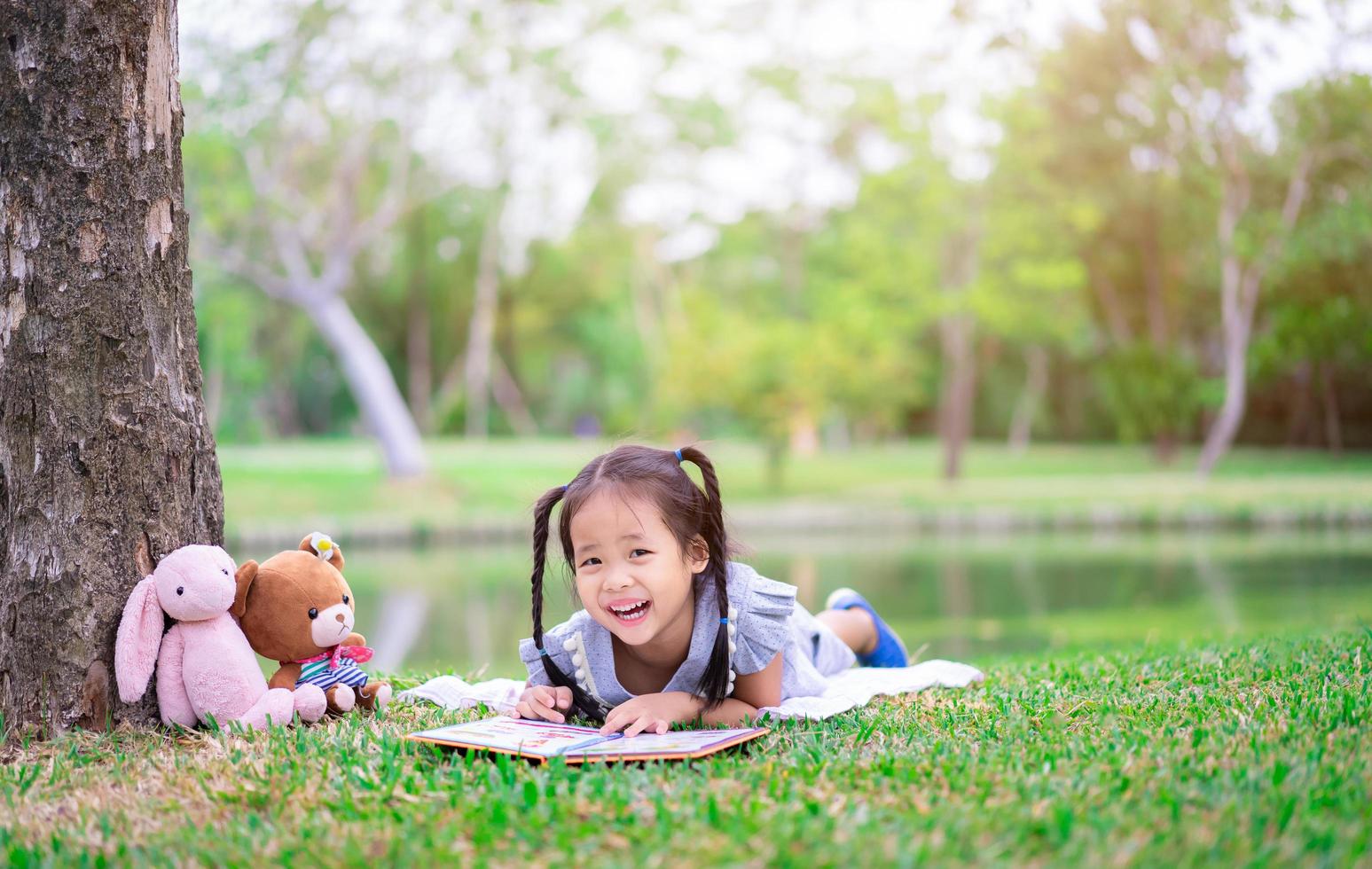 junges Mädchen im Park mit Buch und Puppen foto