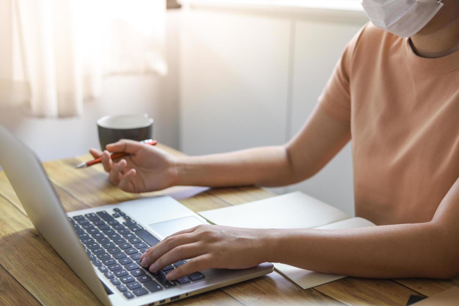 Frau, die von zu Hause auf Laptop mit Gesichtsmaske arbeitet foto