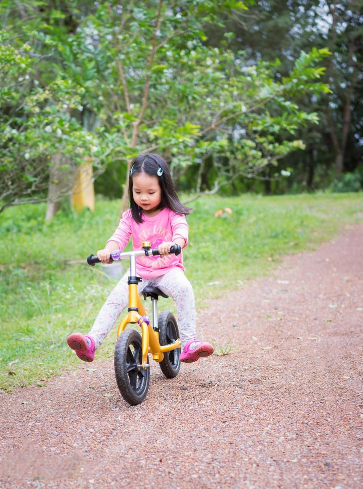 kleines Mädchen lernt, im Park Laufrad zu fahren foto