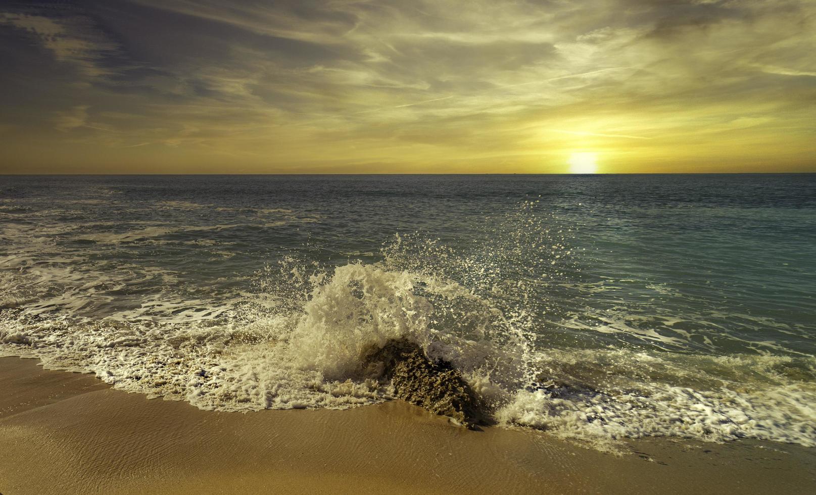 Wellen plätschern am Strand bei Sonnenuntergang foto