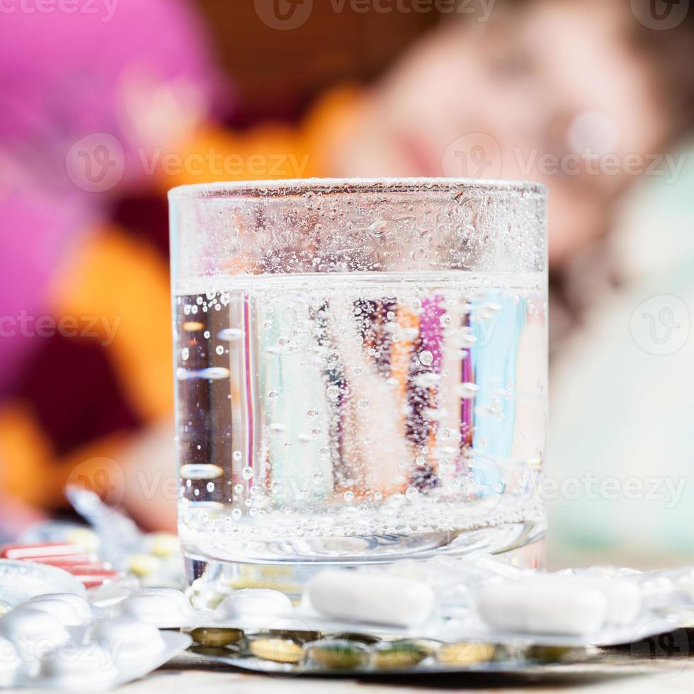 Glas mit gelöstem Medikament und Pillen auf dem Tisch foto