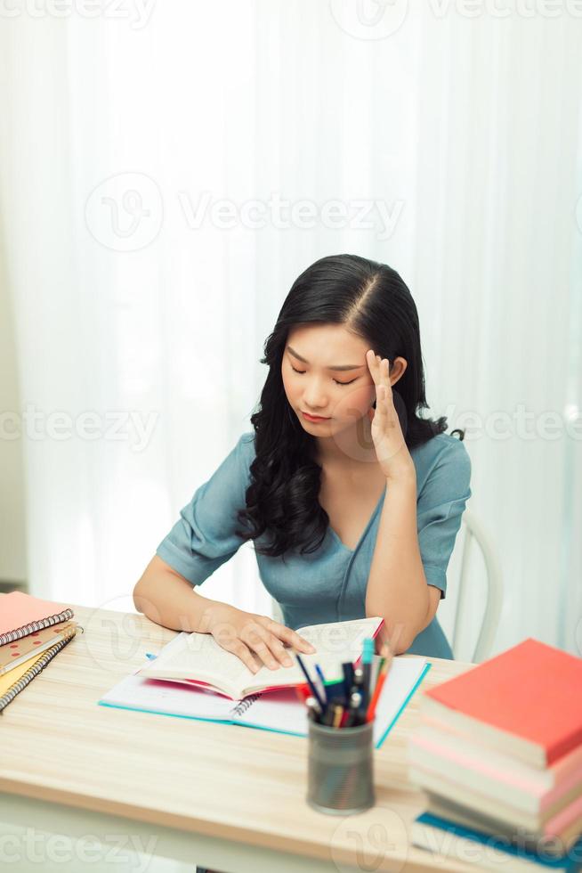 fokussiertes schulmädchen, das mit büchern studiert, die sich auf die prüfungsprüfung vorbereiten und essay schreiben, das zu hause hausaufgaben macht foto