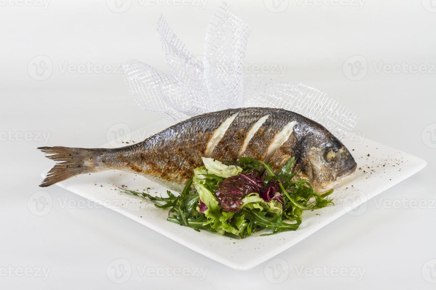 Dorada-Fisch mit Salat auf dem weißen Teller. Studioaufnahme foto