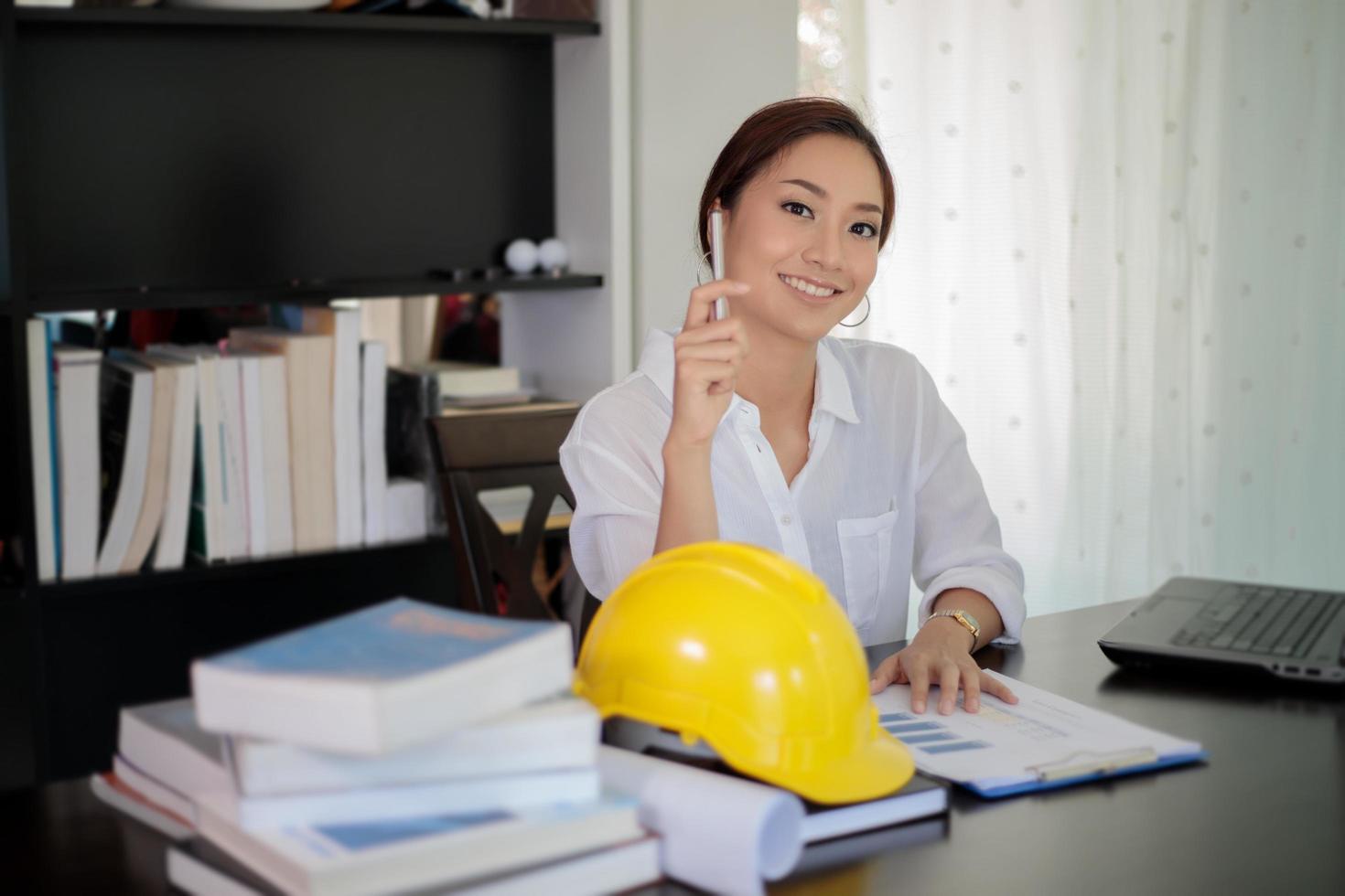 asiatische Frau mit Schutzhelm und Zwischenablage im Büro foto