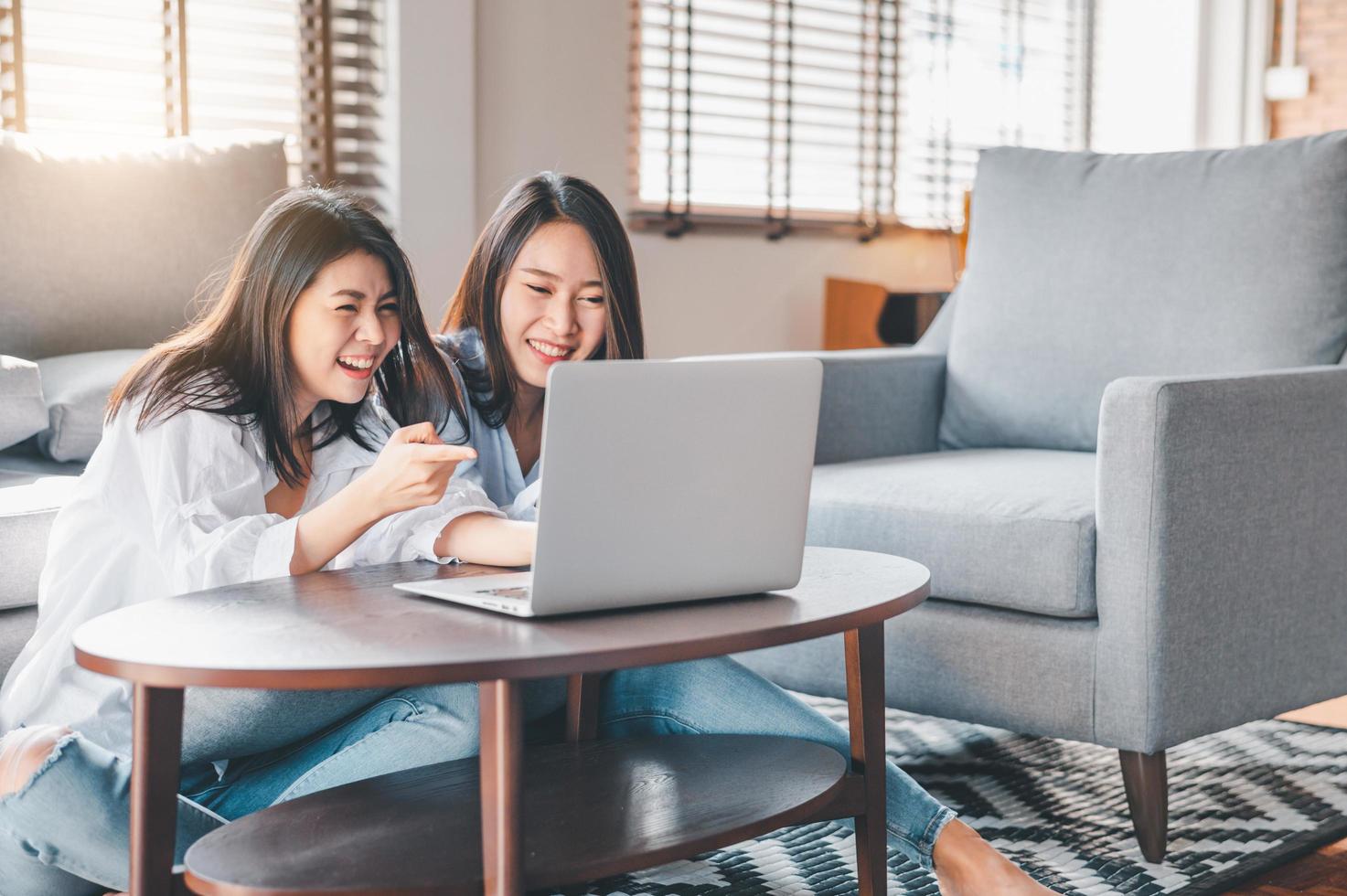 zwei glückliche asiatische Frauen lachen, während sie mit Laptop zu Hause arbeiten foto