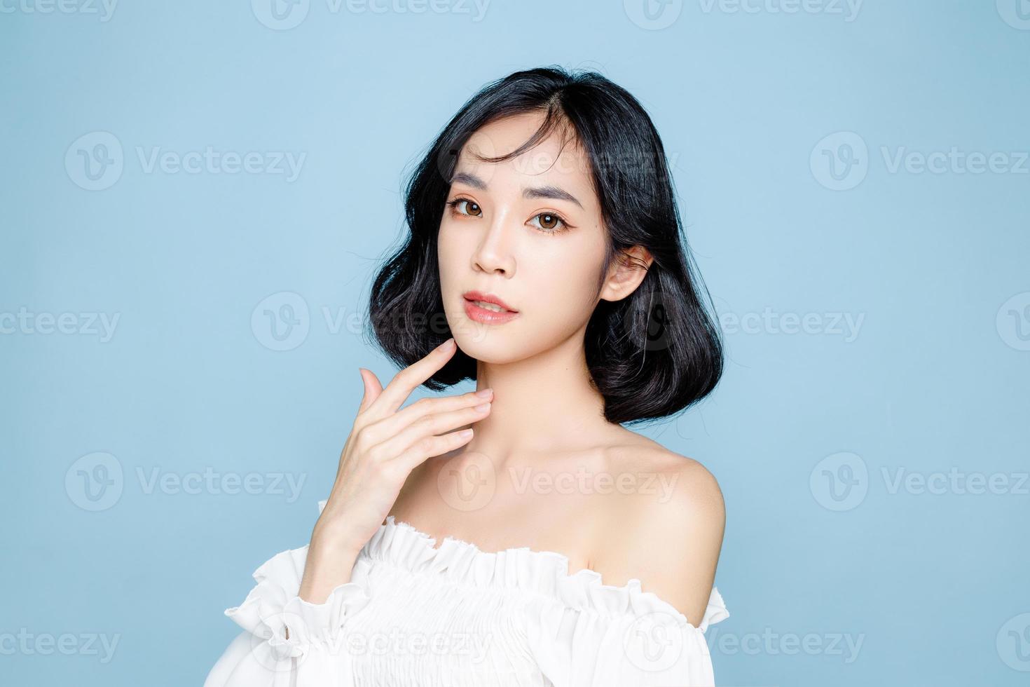 kurze haare der asiatischen frau mit perfekter sauberer frischer haut. süßes weibliches Modell mit natürlichem Make-up und funkelnden Augen auf blauem, isoliertem Hintergrund. gesichtsbehandlung, kosmetik, schönheitskonzept. foto