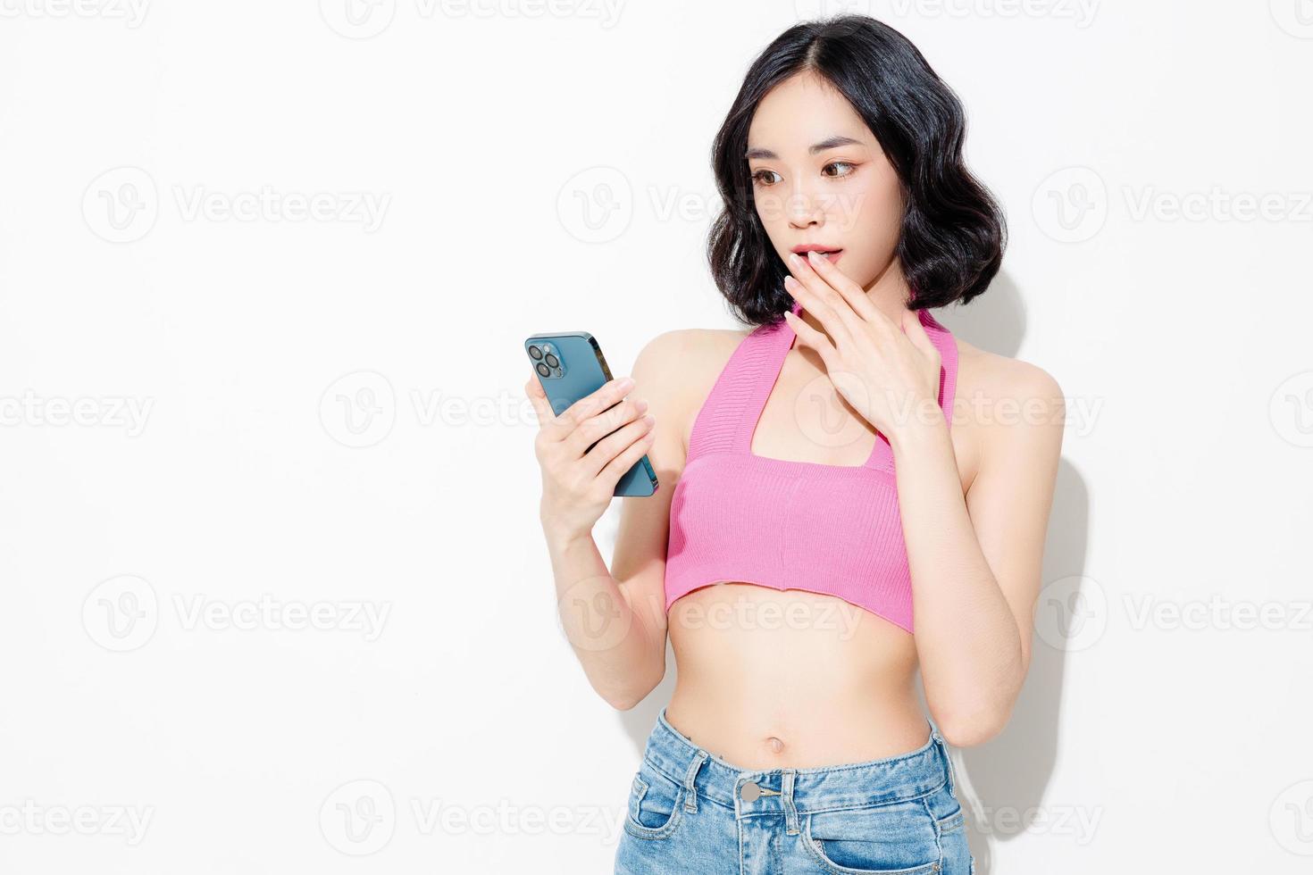 modische asiatische Frau kurze Haare mit perfektem Körper mit Handy. süßes weibliches Model und funkelnde Augen auf weißem, isoliertem Hintergrund. gesichtsbehandlung, kosmetik, schönheitskonzept. foto