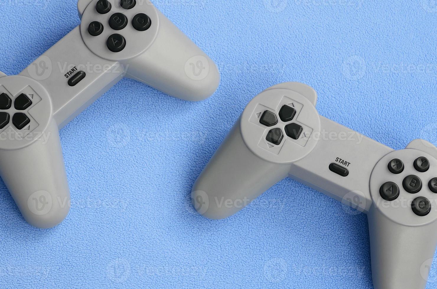 Spielkonzept spielen. Zwei Pad-Joysticks liegen auf der Decke aus pelzigem blauem Fleece-Stoff. Controller für Videospiele auf einer Hintergrundstruktur aus hellblauem, weichem Plüsch-Fleece-Material foto