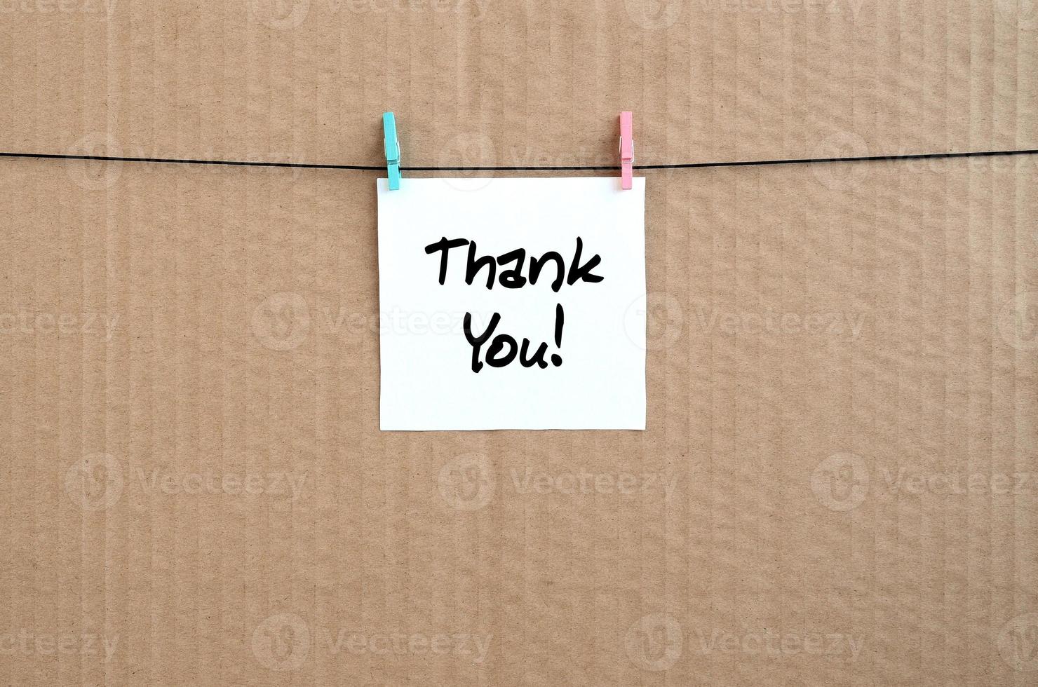 Dankesschreiben steht auf einem weißen Aufkleber, der mit einer Wäscheklammer an einem Seil auf einem Hintergrund aus braunem Karton hängt foto