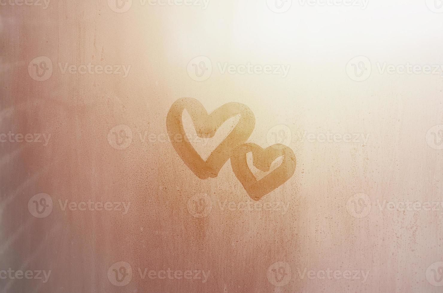 Ein paar abstrakte unscharfe Liebesherzsymbole, die von Hand auf das nasse Fensterglas mit Sonnenlichthintergrund gezeichnet wurden. vorlage für valentinstagpostkarten foto