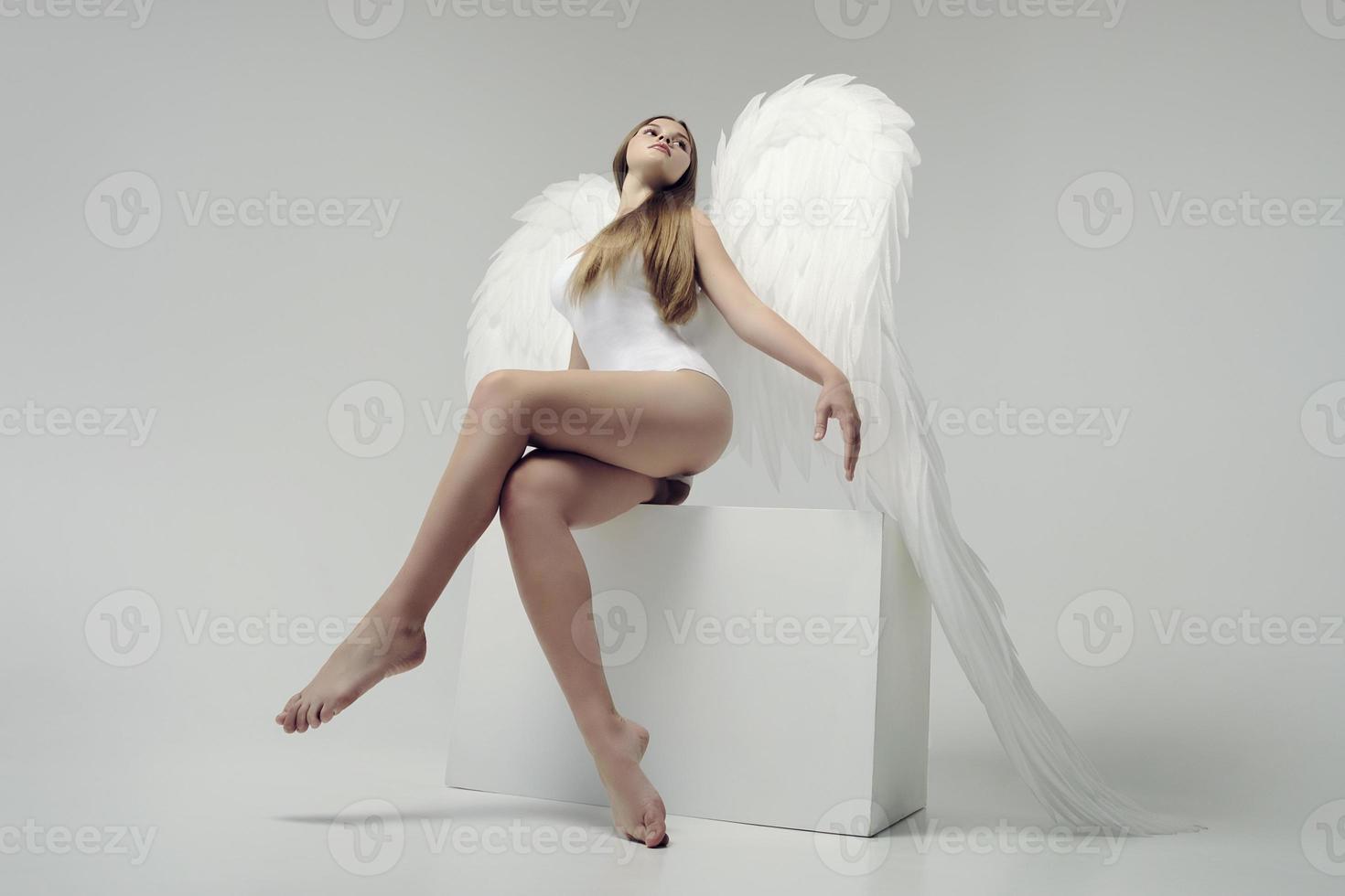 ein romantisches engelsmädchen mit weißen flügeln posiert sitzend foto