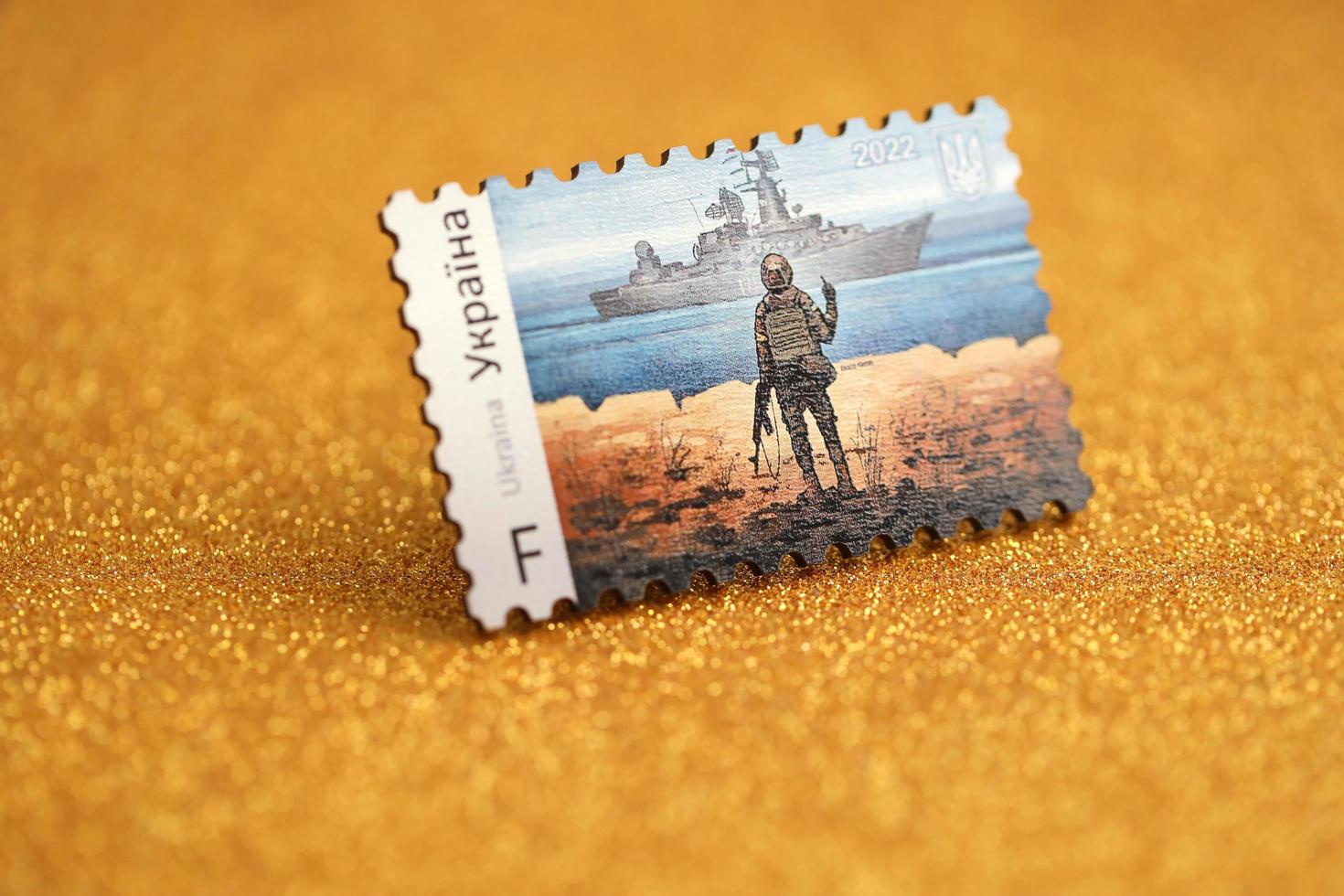 ternopil, ukraine - 2. september 2022 berühmter ukrainischer poststempel mit russischem kriegsschiff und ukrainischem soldaten als souvenir aus holz auf goldenem glitzerhintergrund foto
