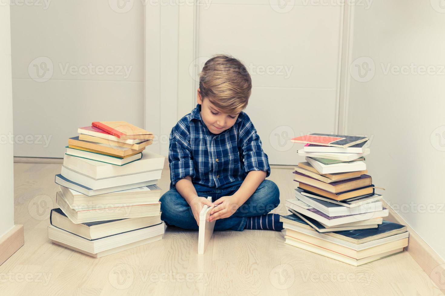 kleiner junge, der unter stapel bücher liest. foto