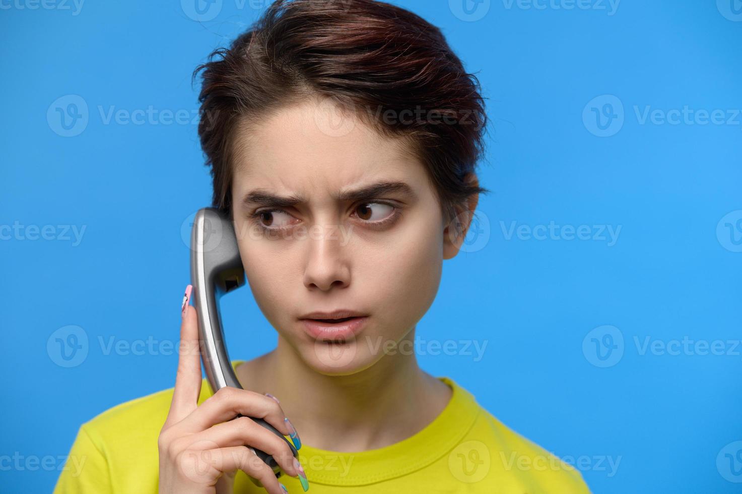 Verärgerte hübsche Brünette, die auf einem Festnetztelefon spricht foto