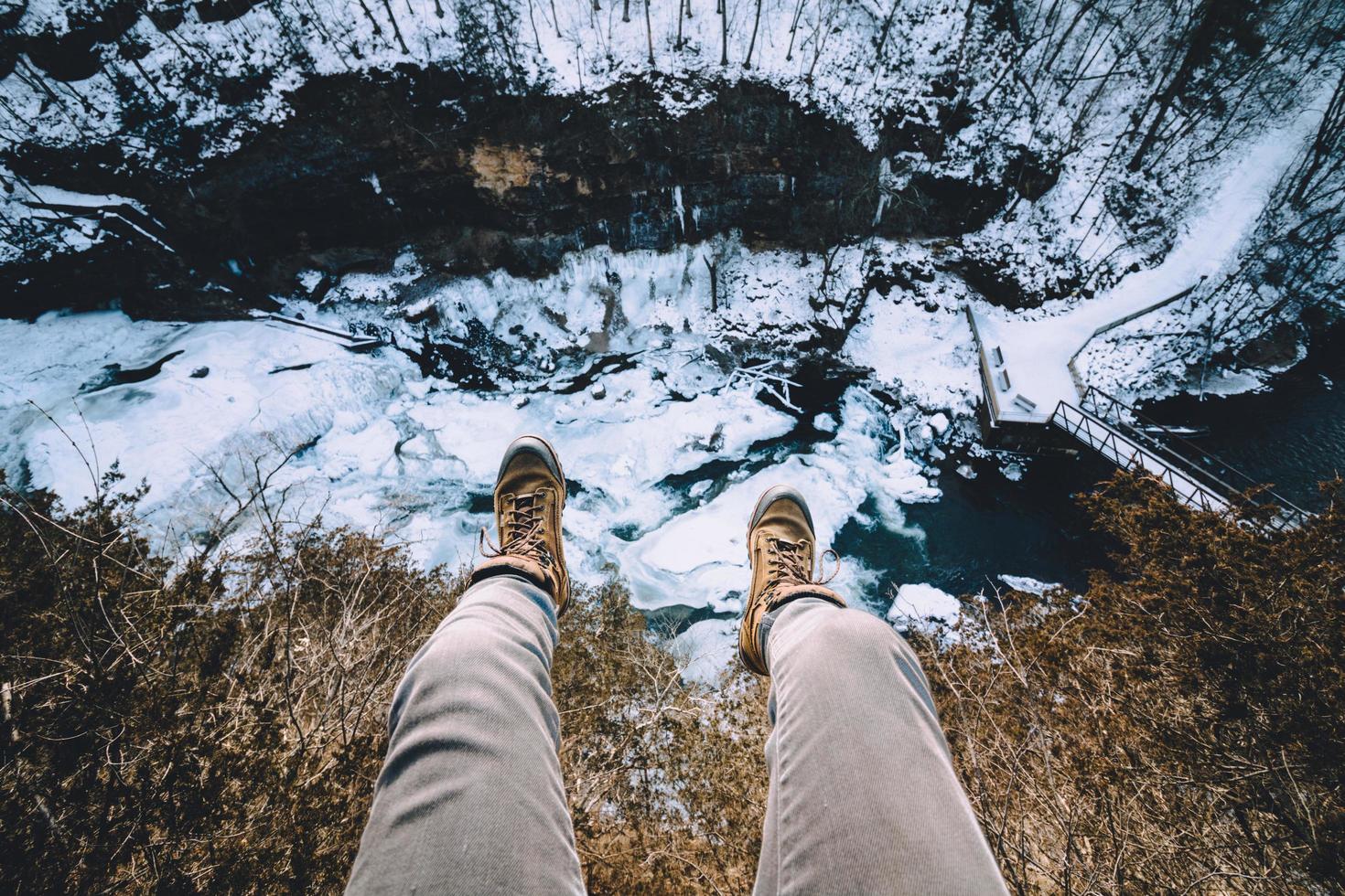 Person, die Beine auf Klippe über gefrorenem Fluss hängt foto