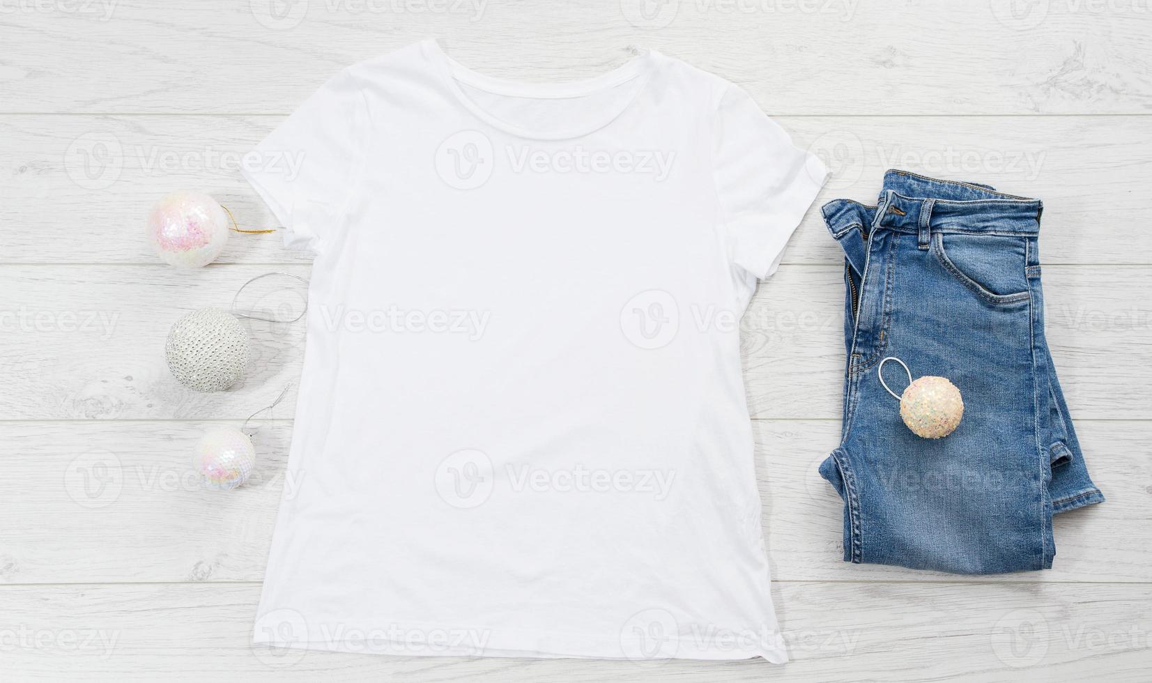 schließen sie herauf weißes leeres schablonen-t-shirt mit kopienraum und weihnachtsfeiertagskonzept. draufsicht-modell-t-shirt und jeans auf weißem hölzernem hintergrund. frohes neues jahr dekorationen zubehör. Weihnachts-Outfit foto