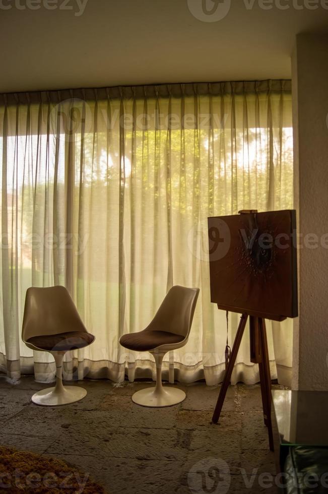 Zimmer mit zwei Stühlen, Vintage-Möbeln, Vorhang dahinter, der das Licht durchlässt foto
