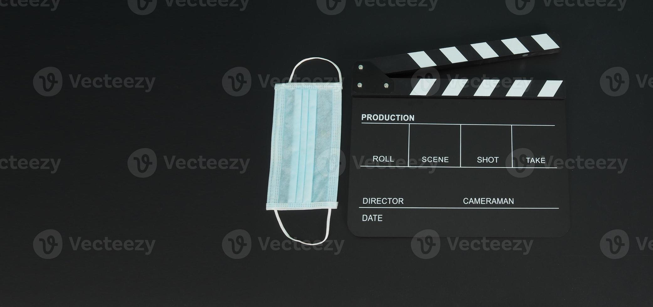 schwarze Klappe oder Filmtafel mit Gesichtsmaske. Es wird in der Videoproduktion, in Filmen und in der Kinoindustrie auf schwarzem Hintergrund verwendet. foto