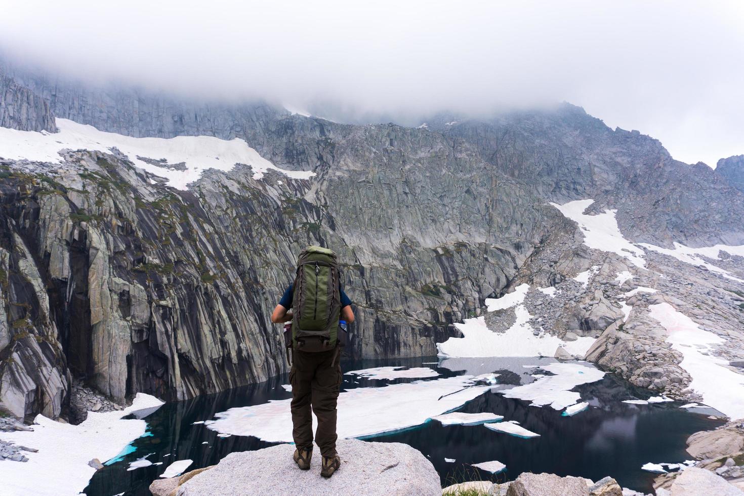 Mann mit Rucksack auf Klippe mit Blick auf Wasser und Berg foto