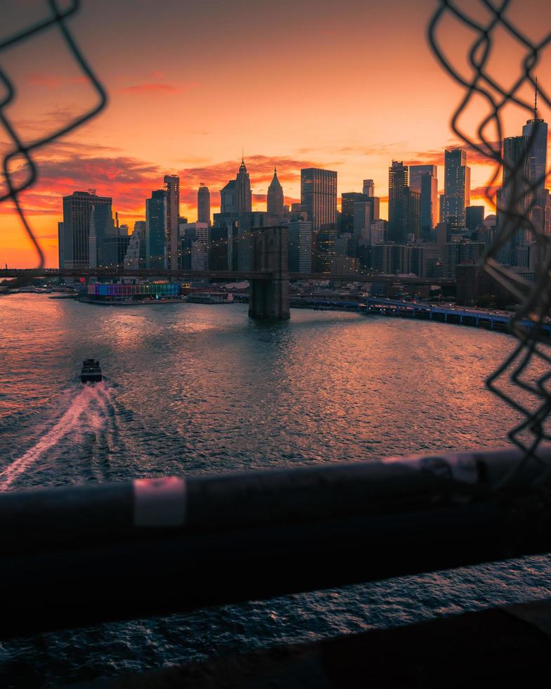 Ein Boot, das unter der Brooklyn Bridge mit der Skyline von New York City vorbeifährt foto