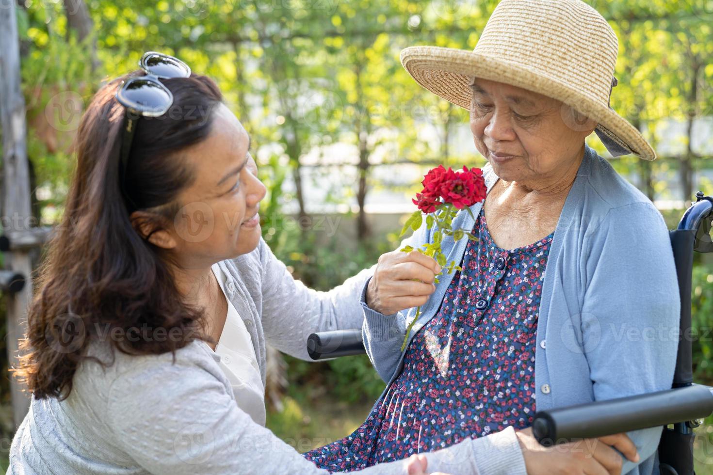 Pflegekraft Tochter umarmt und hilft asiatischen Senioren oder älteren alten Damen, die eine rote Rose auf dem Rollstuhl im Park halten. foto