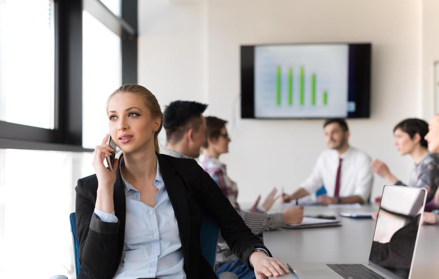 geschäftsfrau, die am telefon im büro spricht, mit team auf treffen im hintergrund foto