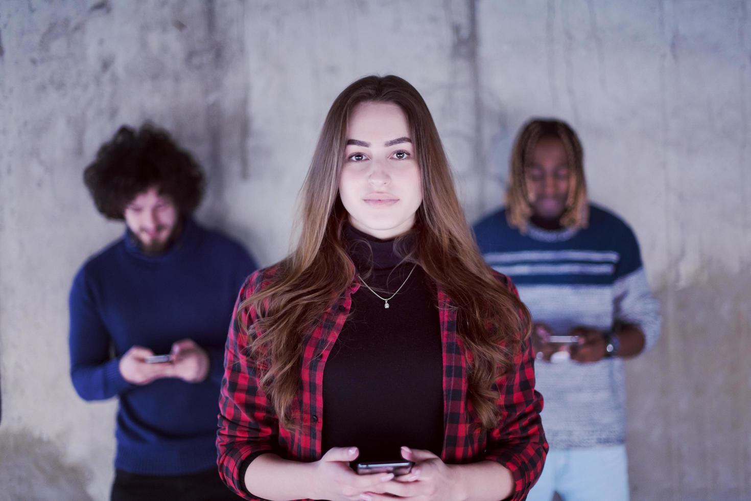 Lässiges multiethnisches Geschäftsteam mit Mobiltelefonen vor einer Betonwand foto