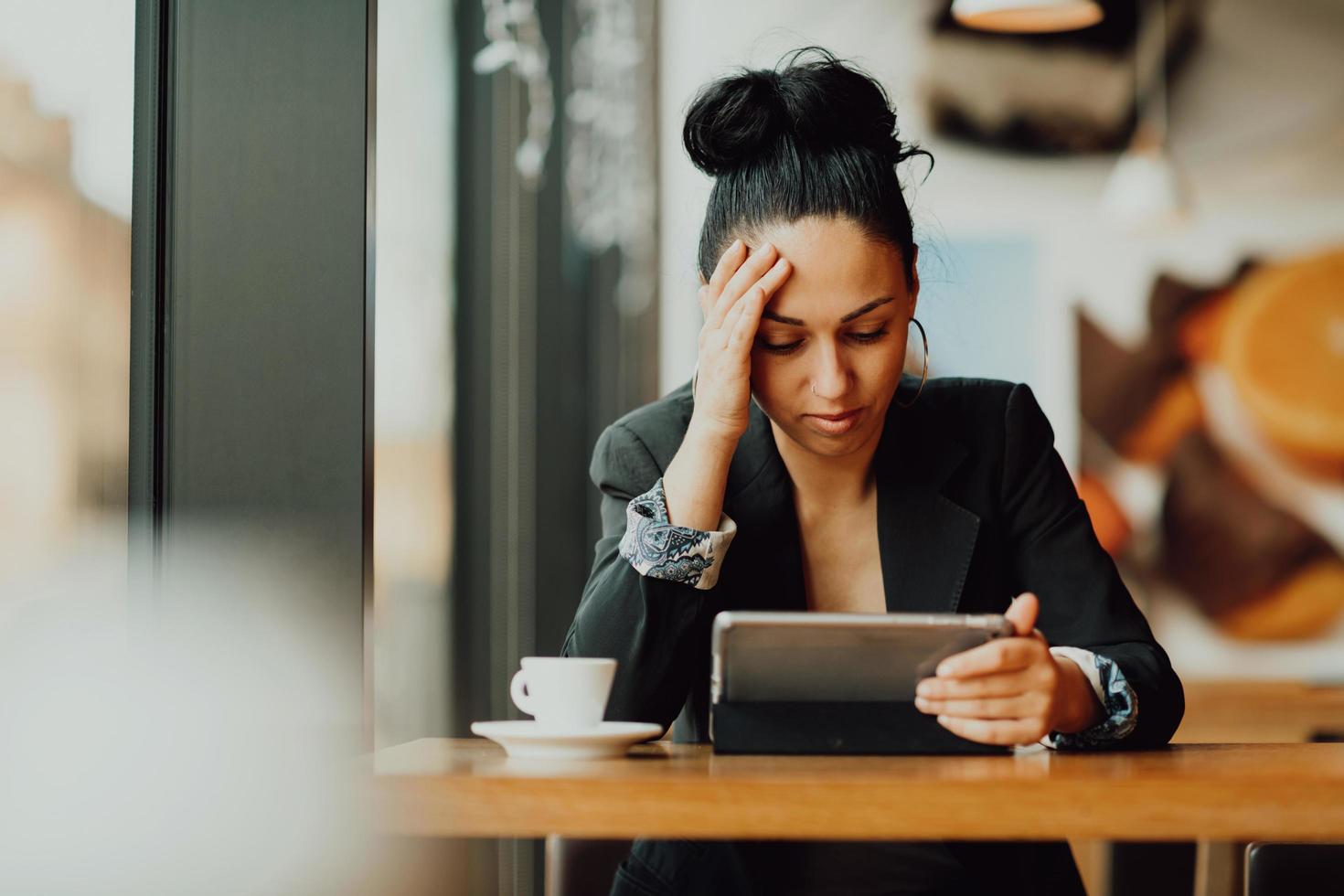 Eine Latina-Frau sitzt in einem Café und blickt enttäuscht auf das Tablet foto