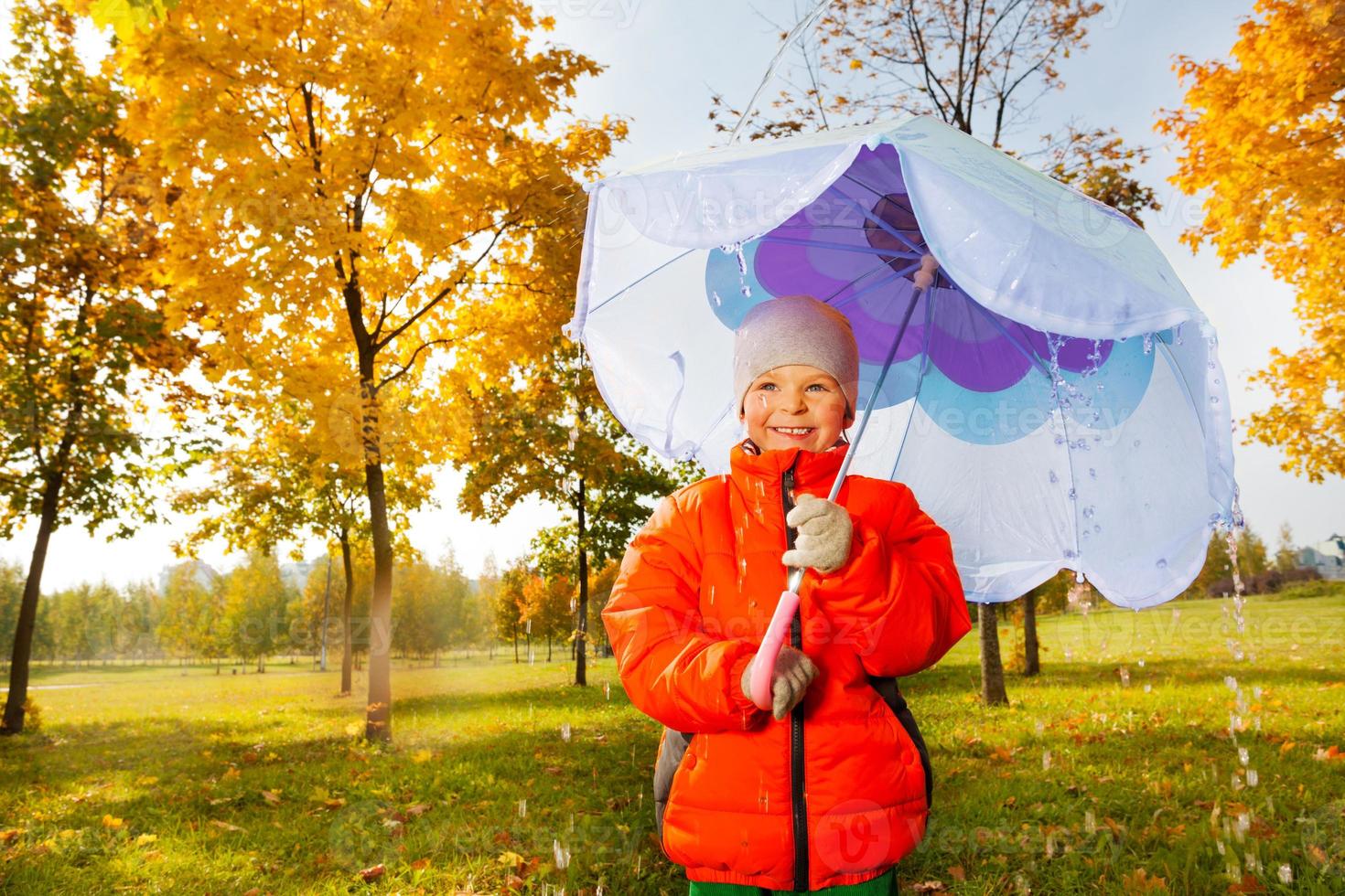 Junge mit blauem Regenschirm steht unter strömendem Regen foto