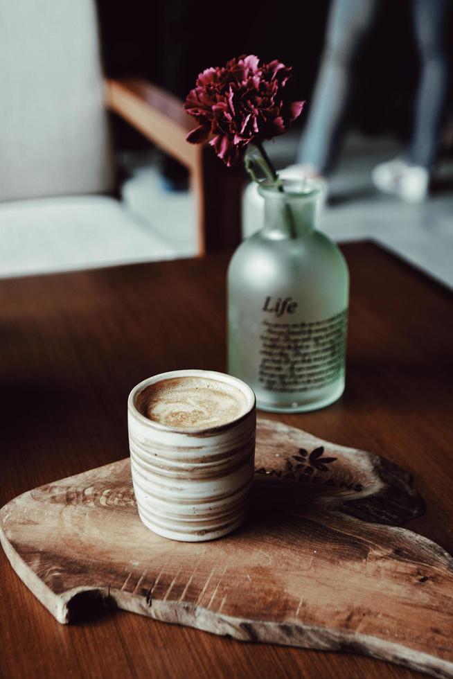 Kaffeetasse auf brauner Holzplatte mit Blumenvase foto