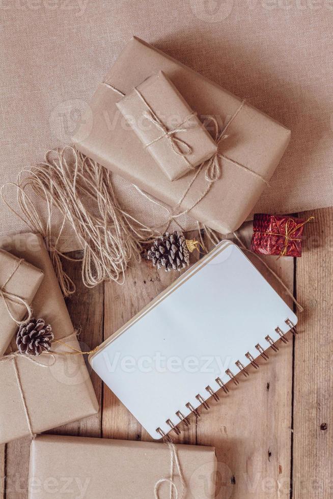 weihnachtsgeschenkbox verwendet braunes recyceltes papier und ein notizbuch und tannenzapfen auf einem holztisch. foto